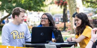 group of three pitt students sitting outside in front of a laptop